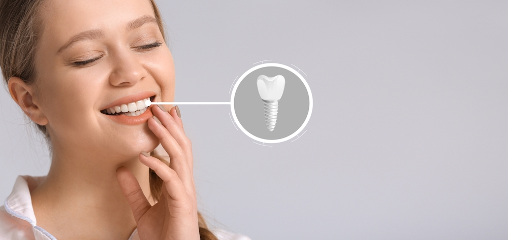 Smiling young woman with implanted teeth on light background